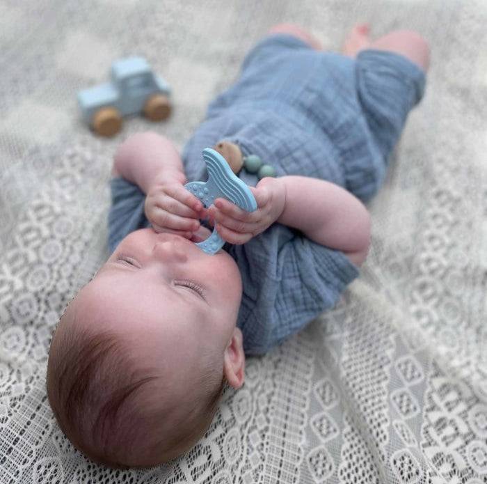 Baby holding Hevea Bumibebe glodalica teether made from natural rubber on a lace blanket.