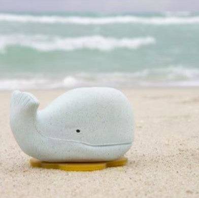 Hevea Squeeze'N'Splash blue whale bath toy made from natural rubber on the beach.