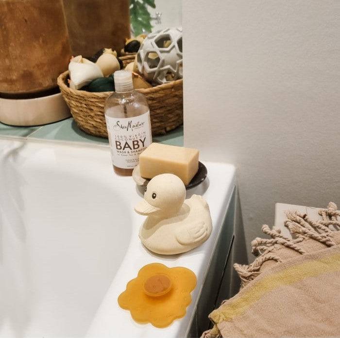 Hevea Squeeze'N'Splash rubber duck bath toy in sand color on bathtub edge.