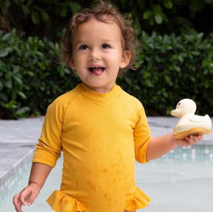 Kid holding Hevea Squeeze'N'Splash rubber duck in sandy color by the pool.