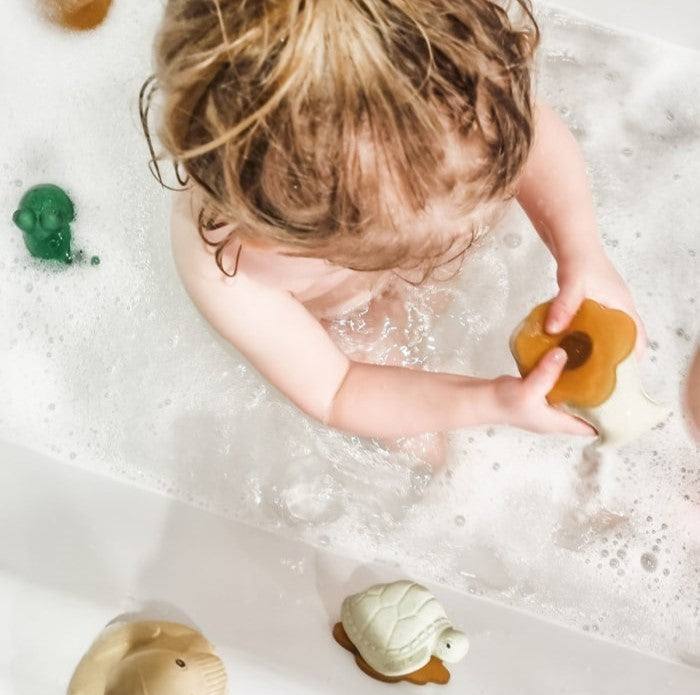 Child playing with Hevea Squeeze'N'Splash bath toys, whale and turtle, in a bubbly bathtub.