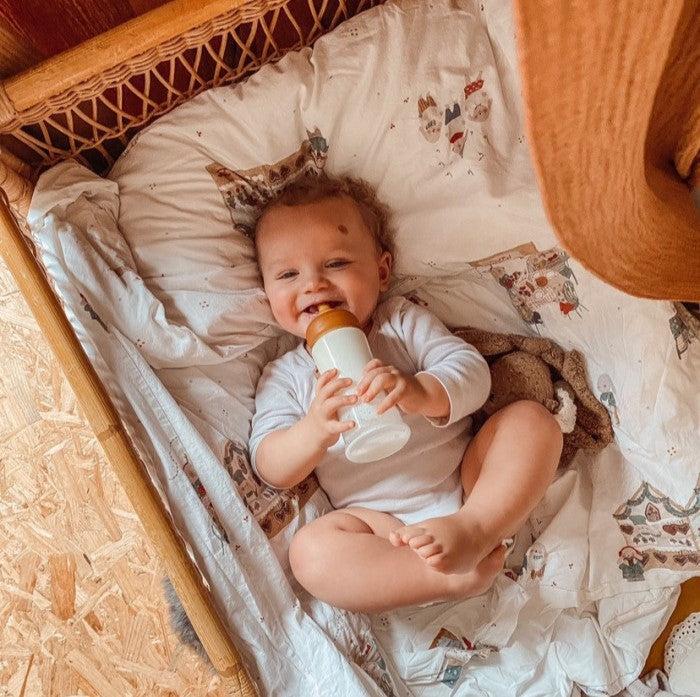 Baby in crib holding a bottle with Hevea cucla za flašice, medium flow nipple.