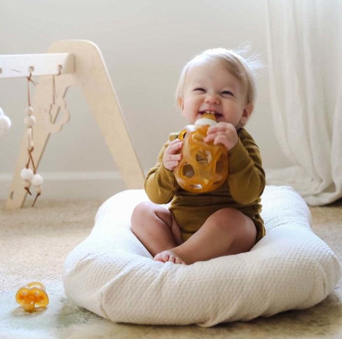 Baby holding Hevea staklena flašica with Star Ball cap in play setting.