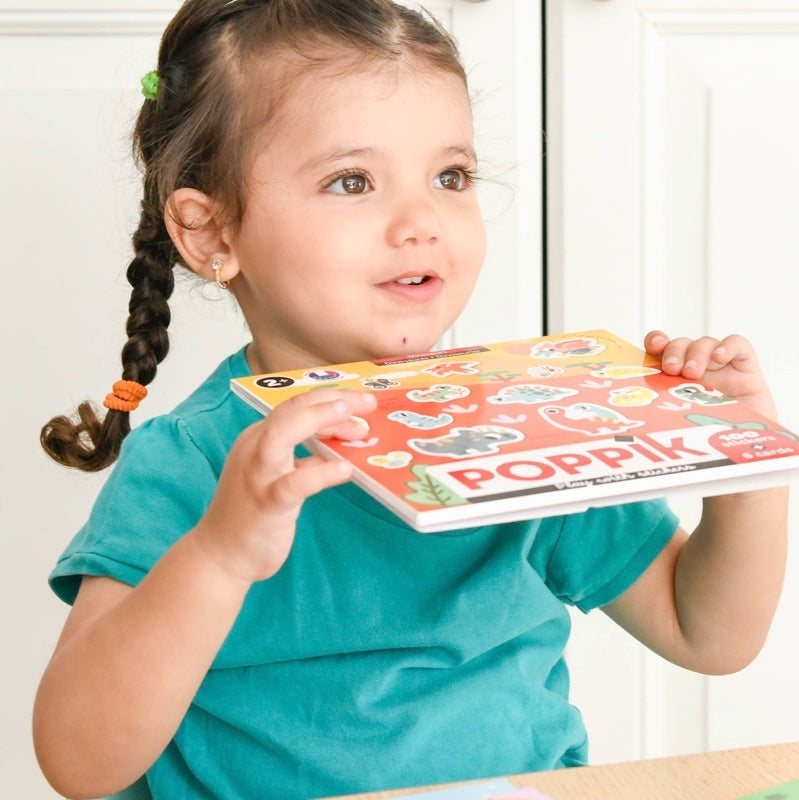 Child holding Poppik Moje prve nalepnice sticker set with vibrant designs.