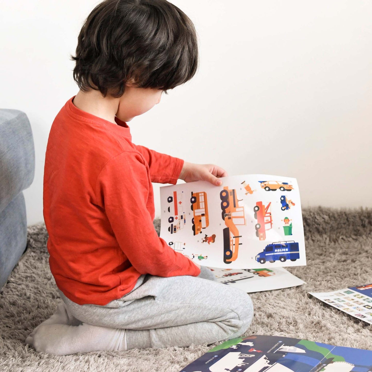 Child playing with Poppik Edukativni poster featuring vehicle stickers on a detailed garage-themed background.