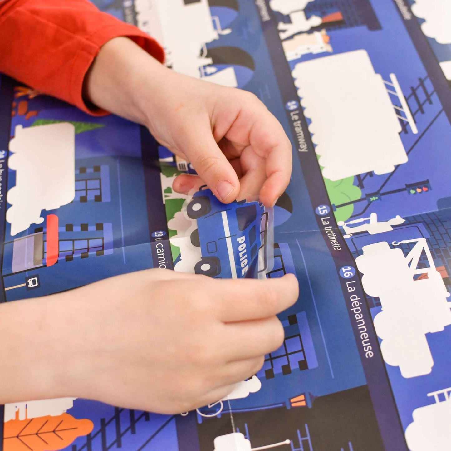 Child placing a vehicle sticker on the detailed Poppik educational poster with multilingual features, for fun learning and vocabulary development.