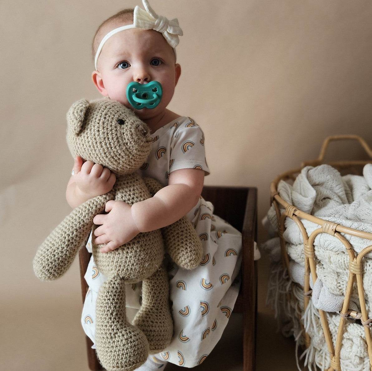 Baby with green Hevea orthodontic pacifier holding a teddy bear.